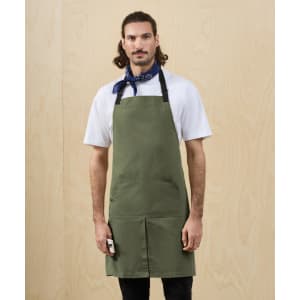 A man wearing a khaki utility apron with pockets, paired with a blue scarf, standing against a wooden backdrop.