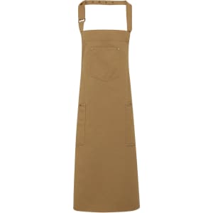 A tan Chino Cotton Bib Apron featuring a pocket and two side pockets, with an adjustable neck strap and a logo.
