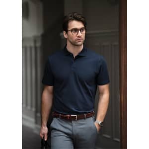 A navy polo shirt worn by a man with glasses, paired with grey trousers and a belt, standing in an outdoor setting.