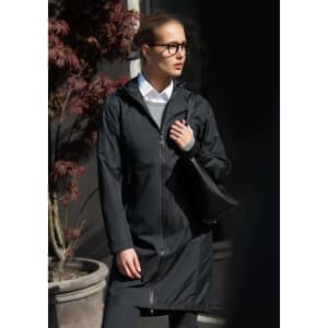 A black rain jacket with a hood, worn by a woman holding a black bag, against a backdrop of plants.