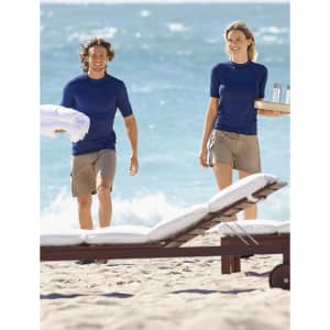 A navy blue short sleeve rash guard worn by a man and woman, walking on a sandy beach with ocean waves in the background.