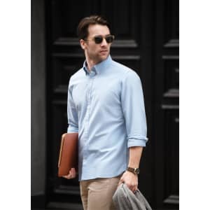 A light blue button-up shirt worn by a man holding a laptop and wearing sunglasses, with rolled-up sleeves.