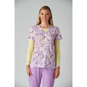 A floral print scrub top in lavender with yellow flowers, paired with a light yellow long-sleeve shirt and purple pants.