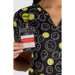 A patterned shirt featuring various smiley faces in yellow and white on a black background, held by a person with a badge.