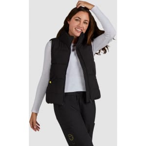 A woman models a black padded vest over a long-sleeve white top, smiling and posing against a plain background.