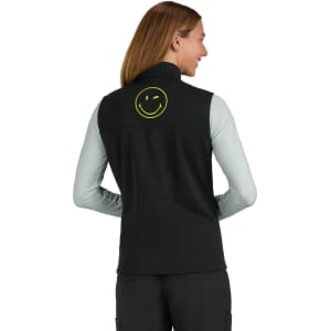 A black fleece vest with a smiley face logo on the back, worn over a light-coloured long-sleeve top.