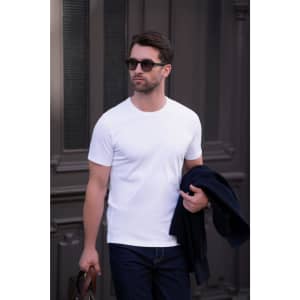 A white men’s T-shirt is displayed, worn by a man carrying a bag and dressed in dark jeans and sunglasses.