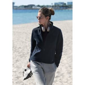A women’s navy jacket with a high collar, paired with grey pants, worn by a model on a sandy beach.