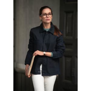 A woman wearing a dark navy jacket with a green top and white pants, holding a notebook and walking.
