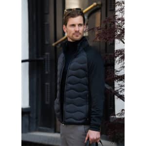 A man wearing a black puffer jacket with a zip front, standing outside near a building entrance.