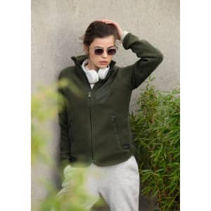 A green women's jacket with a zip front and pockets, worn over a grey hoodie, paired with sunglasses and headphones.