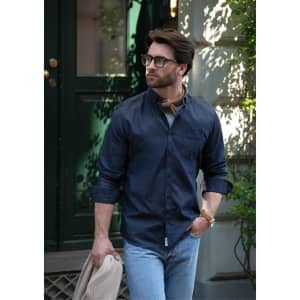 A slim fit men's button-up shirt in navy, paired with light jeans and a beige jacket, featuring a logo.