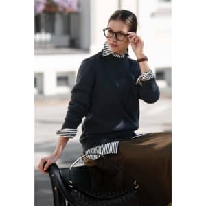 A dark grey unisex sweatshirt worn over a striped shirt, paired with a long skirt and accessorised with glasses.
