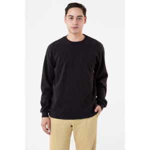 A man wearing a black heavyweight thermal crewneck jumper paired with beige trousers. The garment has a logo on it.