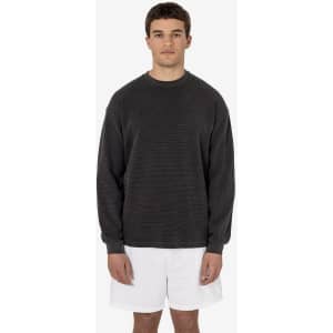 A man wearing a dark grey heavy thermal crewneck jumper and white shorts, standing against a plain background.