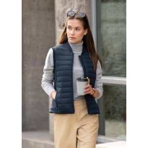 A navy women's vest with a lightweight design, paired with a grey turtleneck and beige pants, featuring a logo.