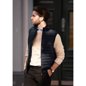 A man wearing a navy puffer vest over a cream sweater, standing outside with a stylish backdrop.
