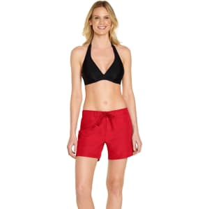A woman models red cargo board shorts, paired with a black halter bikini top. The shorts feature a drawstring waist and a logo.