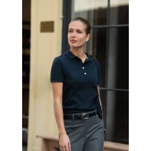 A woman in a navy polo shirt walks confidently, paired with grey trousers and a sleek hairstyle. The shirt has a logo.