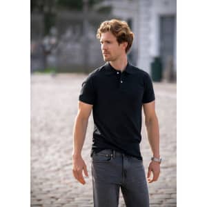 A black polo shirt worn by a man with wavy hair, paired with grey jeans, standing outdoors. The shirt features a logo.