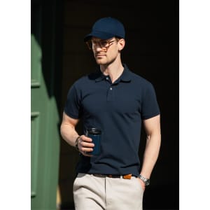 A navy polo shirt worn by a man holding a drink, paired with a matching cap and light trousers.