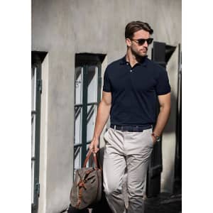A navy polo shirt worn with beige trousers, complemented by sunglasses and a brown bag, set against a street backdrop.