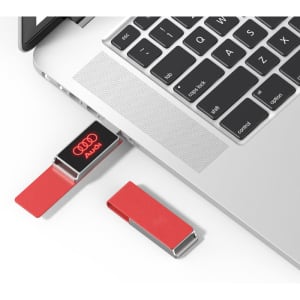 A red Milan LED flash drive is connected to a laptop, with another red flash drive nearby. The product features a logo.