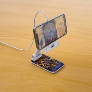 A white magnetic wireless charger with a phone propped up, featuring a colourful design on the charging surface.