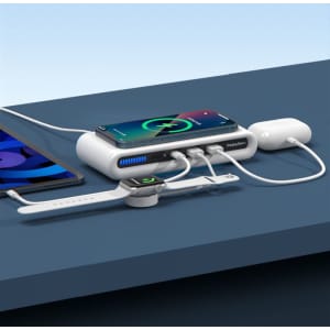 A white wireless charging station with a phone, smartwatch, and earbuds connected by cables, placed on a blue surface.