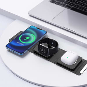 A black wireless charger with three sections, charging a phone, smartwatch, and earbuds on a light surface.