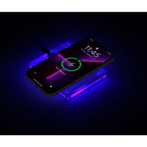 A wireless charger with a sleek acrylic design in purple, featuring a smartphone displayed on top, illuminated by soft light.