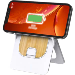 A wireless charging stand in white and bamboo, holding a smartphone displaying a full charge indicator.