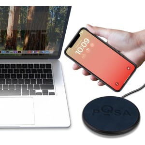 A wireless charger with a circular design in black, positioned next to a laptop and a smartphone.