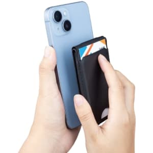 A black magnetic card wallet is being held against a smartphone, with credit cards inserted into the wallet.