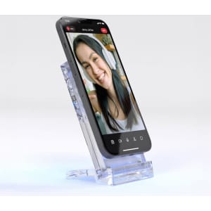 A clear acrylic wireless charging stand displaying a smartphone in a vertical position, featuring a smiling face on the screen.