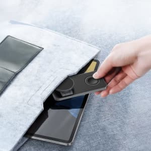 A grey 15W 3-in-1 magnetic wireless charging station being taken from a pocket, with a tablet visible below.