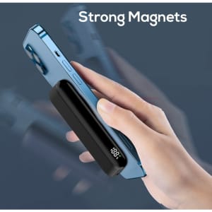 A black magnetic power bank with a digital display, being held next to a blue phone.