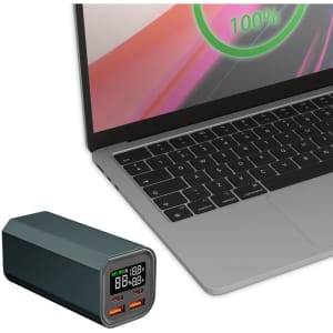 A green power bank with digital display sits next to a laptop, featuring USB ports for charging.