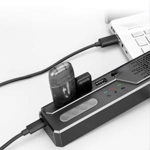 A black Akron Omnidirectional Speaker Phone connected to a laptop, featuring buttons and ports for connectivity.