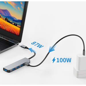 A silver USB hub with multiple ports connects to a laptop and a power adapter, displaying black cables and accessories.