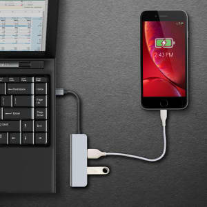 A Type-C hub in grey connecting a laptop to a phone, with a visible power source and a charging indicator on the phone.