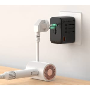 A black travel adaptor with multiple ports is plugged into a wall socket, connected to a white device.