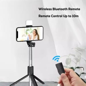 A black LED selfie stand with a smartphone mounted on it, featuring a wireless Bluetooth remote and extendable legs.