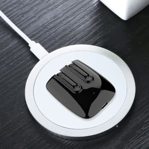 A pair of black magnetic TWS earbuds resting on a round charging pad on a wooden surface.