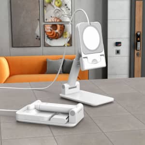 A white foldable phone stand with an adjustable clip and a base, placed on a countertop beside an orange couch.