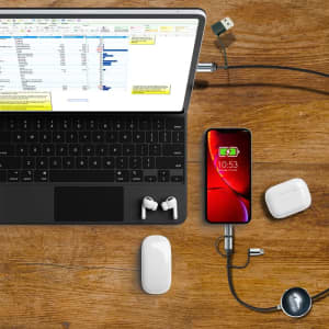 A charging cable with a sleek design connects a smartphone to a laptop, accompanied by wireless earbuds on a wooden surface.