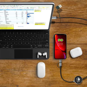 A fast charge and data sync LED cable connects a phone to a laptop on a wooden surface, with earbuds nearby.