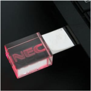 A transparent pink 3D crystal flash drive is inserted into a laptop USB port. The device has a logo.