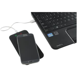 A black wireless charger with a smartphone on top, placed next to a laptop keyboard.