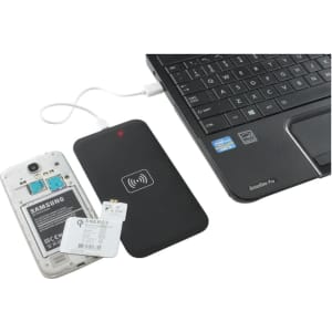 A wireless charger in black connected to a laptop, with a smartphone's back cover removed nearby.